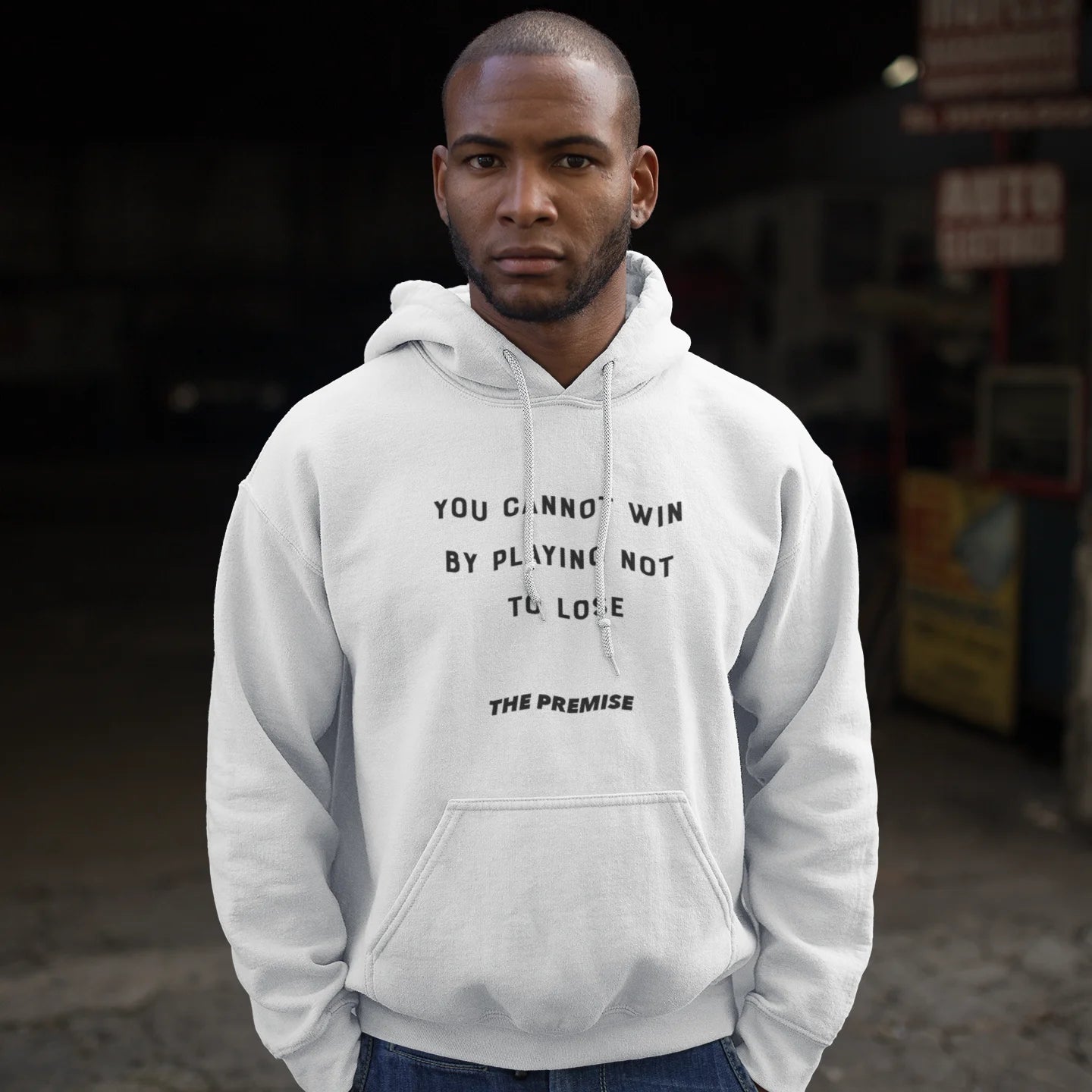 Man in white hoodie with a fearless message about playing to win, standing strong in an urban garage setting.