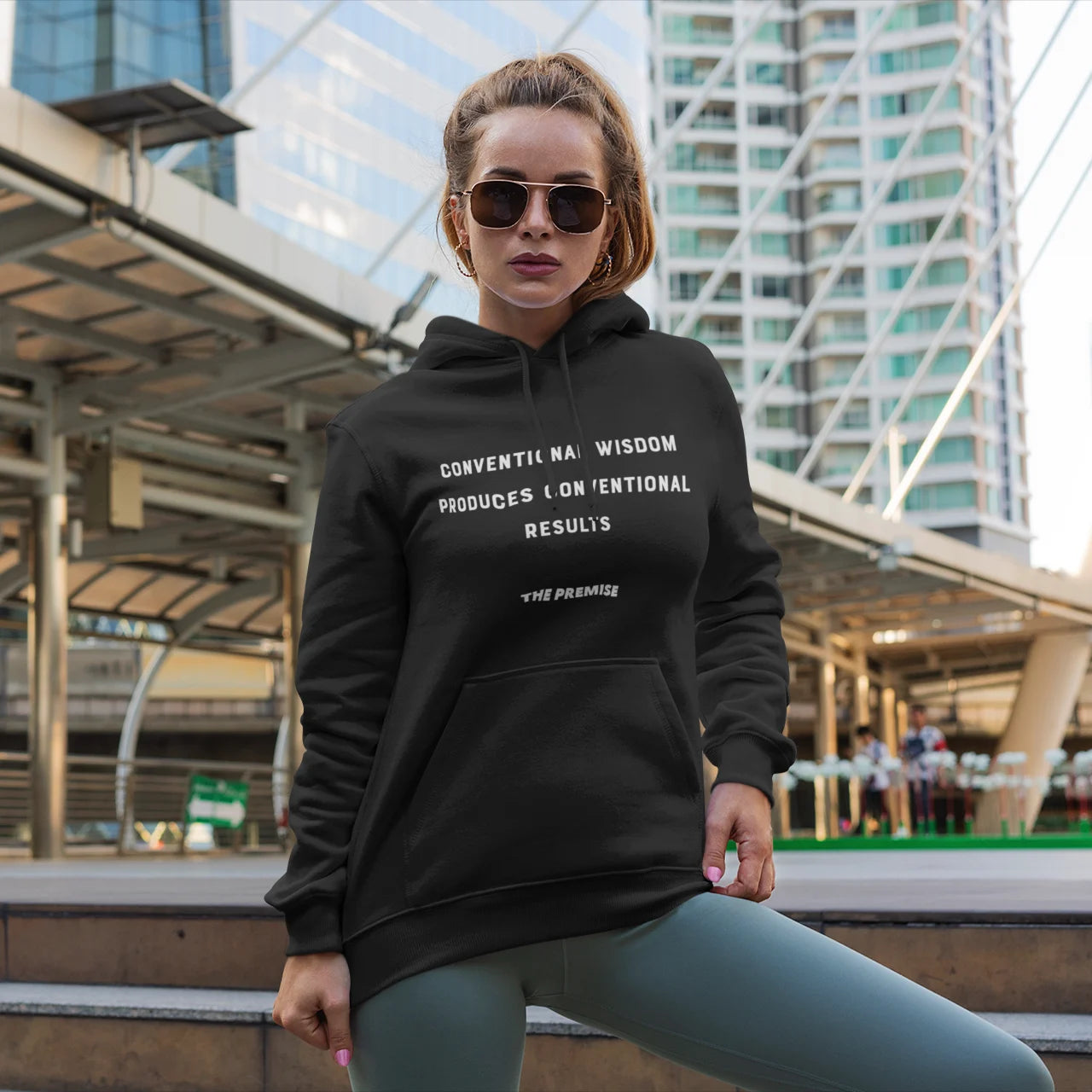 Woman in a black "Break the Mold" hoodie, posing in front of a cityscape with modern glass buildings.