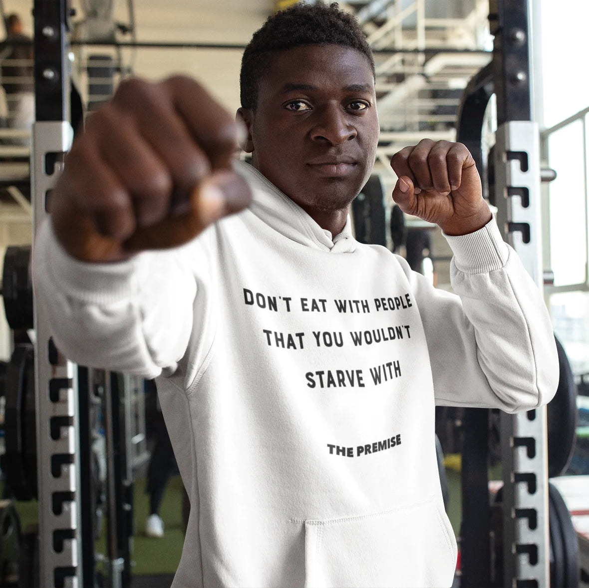 Athlete wearing a white hoodie with motivational text in a gym, representing resilience and ambition.