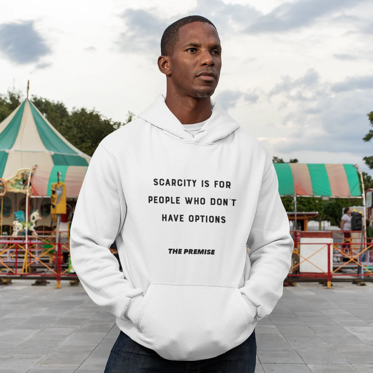 Man in a white hoodie standing strong at a fairground, symbolizing focus and determination.